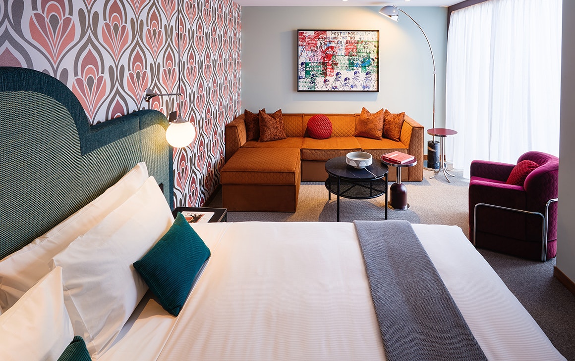 A plush king bed sits against a pink patterned wallpaper inside a suite at the Ovolo South Yarra