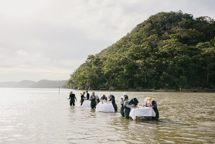 People dining and shucking oysters in the water at tables on the Hawkesbury River. 