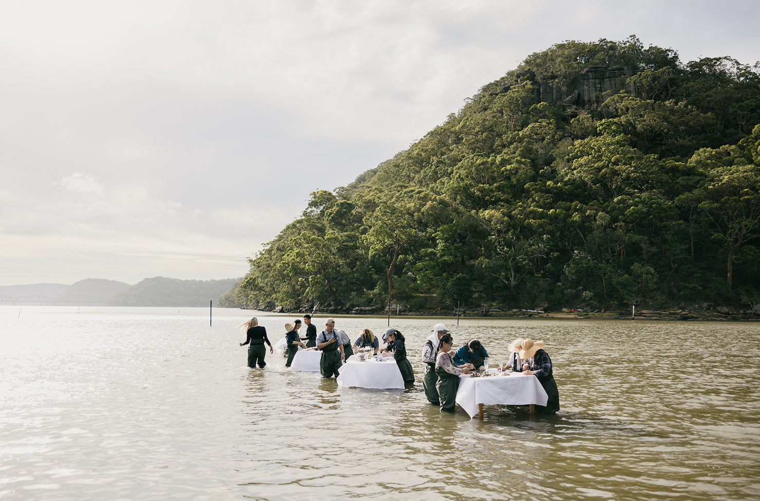 People dining and shucking oysters in the water at tables on the Hawkesbury River. 