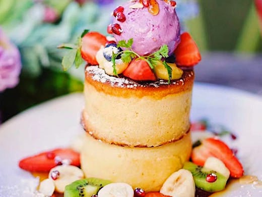 fluffy pancake stack from paddock on crwon cafe, pancakes are decorated in fruit, syrup and ube ice cream