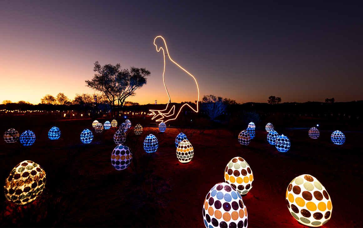 Illuminated yellow and blue Emu eggs are scattered around the red dirt of Alice Springs