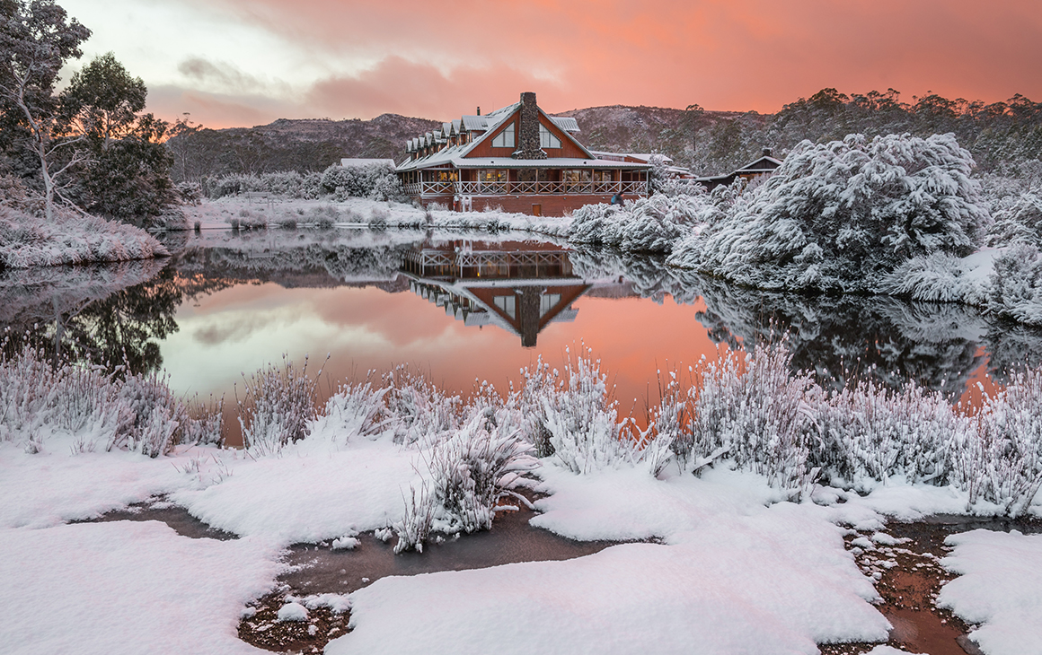 A dusty peach sky and a snow-capped Peppers Resort at Cradle Mountain