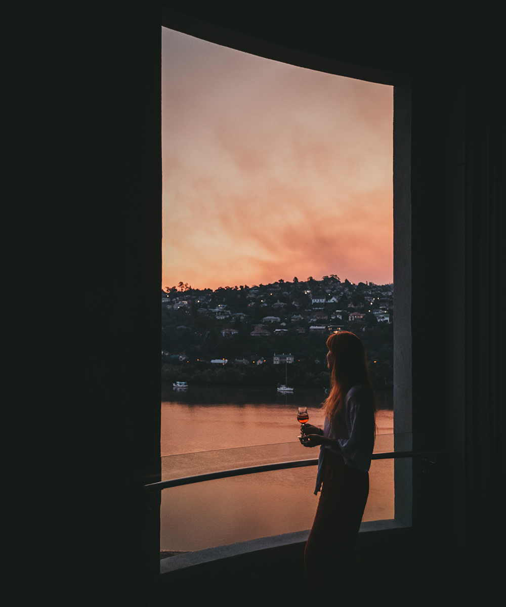 A woman, holding a glass of wine, looks out of Peppers Silo at sunset.