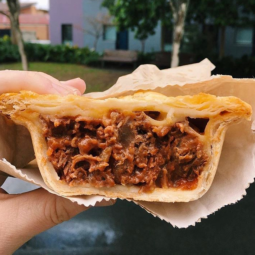 hand holding delicious looking meat pie, cut in half so the fillings can be seen