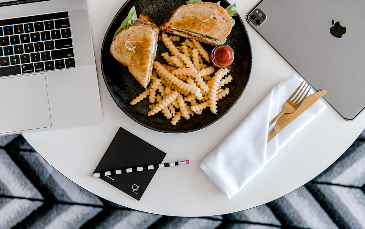 a club sandwich and fries on a plate on a table, in between two laptops