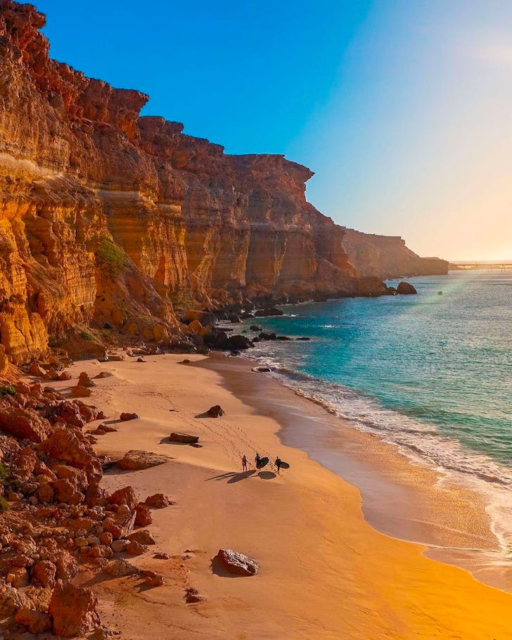 people walking along a rocky coastline with surfboards at sunset