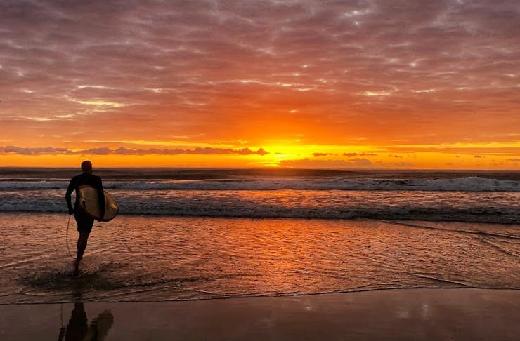 man holding surfboard running into the ocean at sunrise