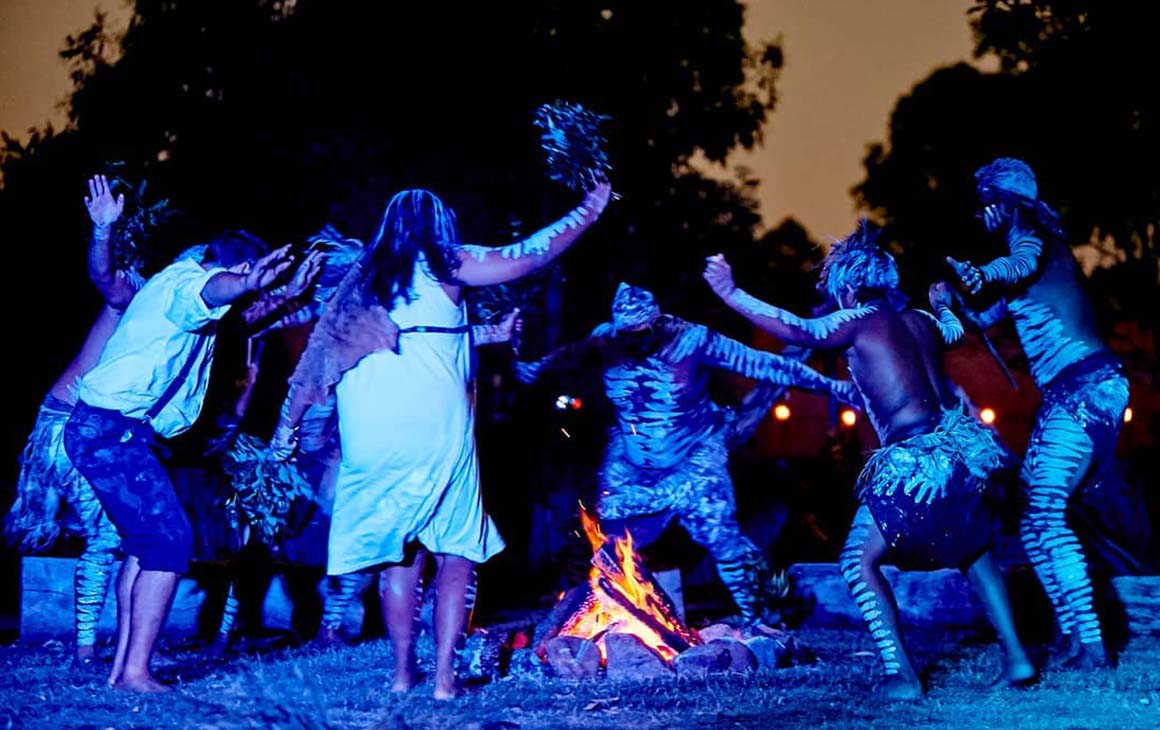a group of First Nations people dance around a fire at night.