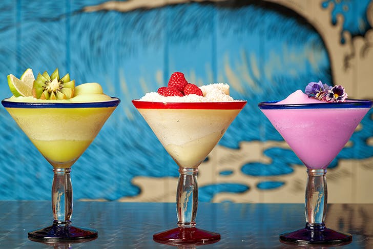 three fruity frozen margaritas lined up on bar top