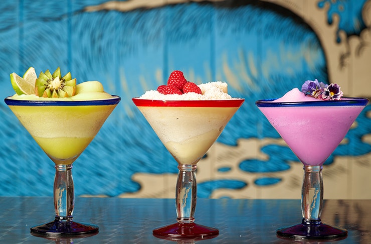 three fruity frozen margaritas lined up on bar top