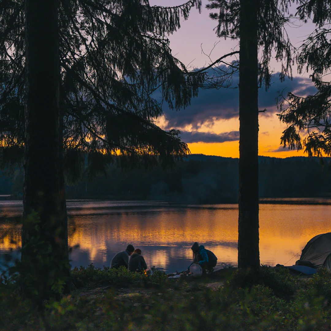 three people camping riverside at sunset