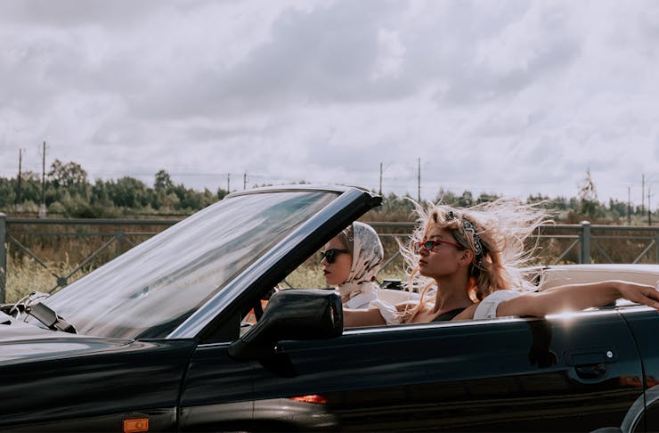 two women drive a convertible with the top down.