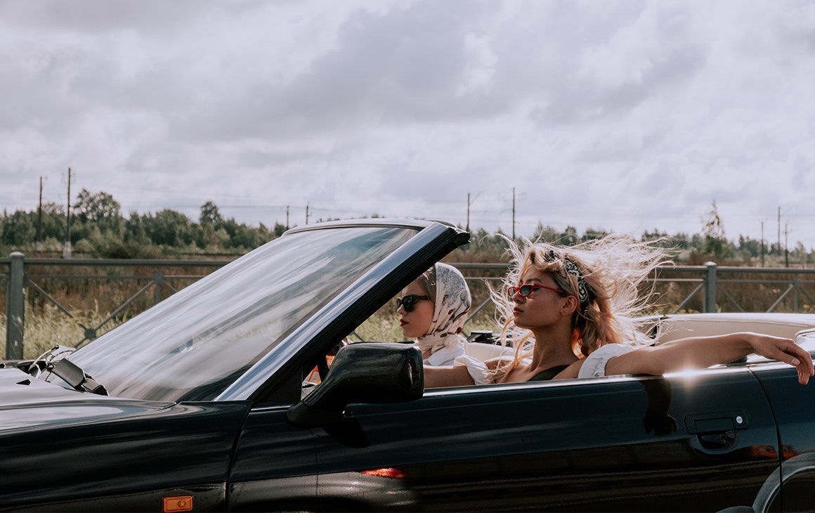 two women drive a convertible with the top down.