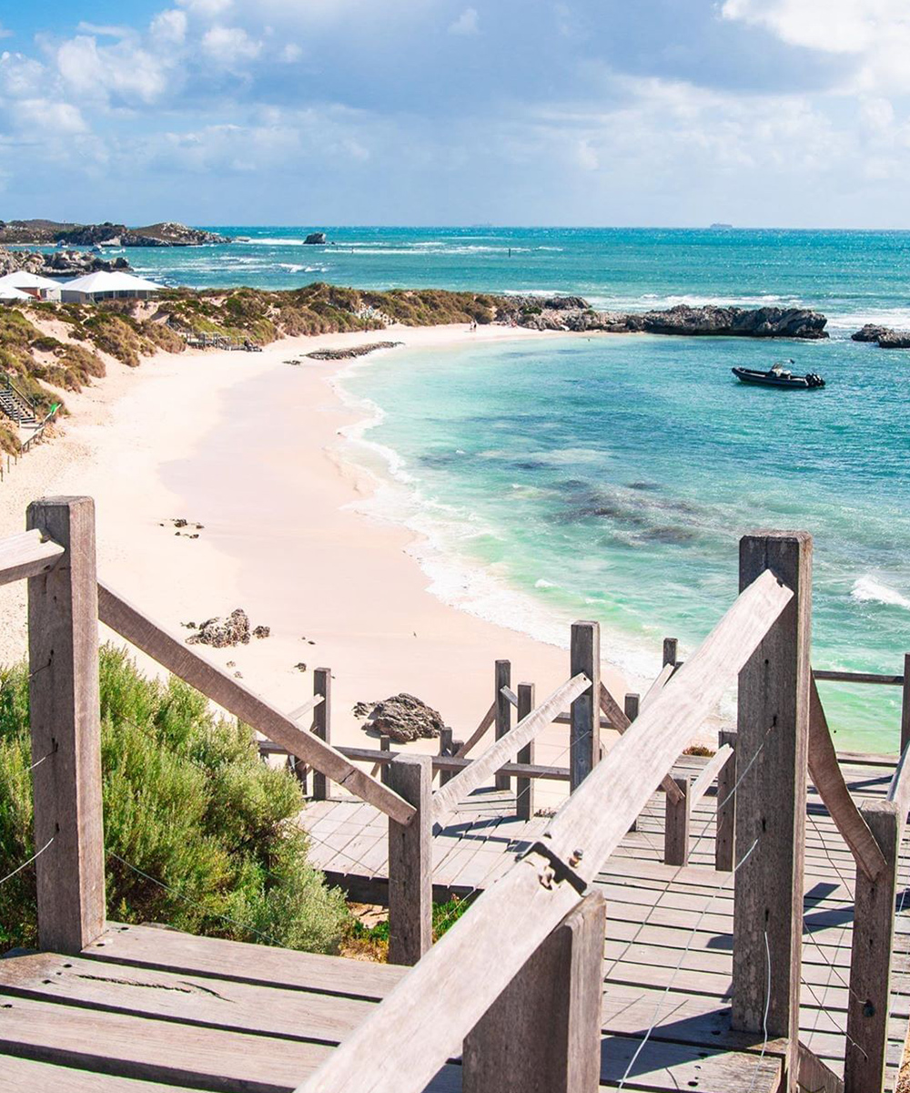 A stunning vista of Pinky Beach at Rottnest Island with white sand, azure water and a blue sky.