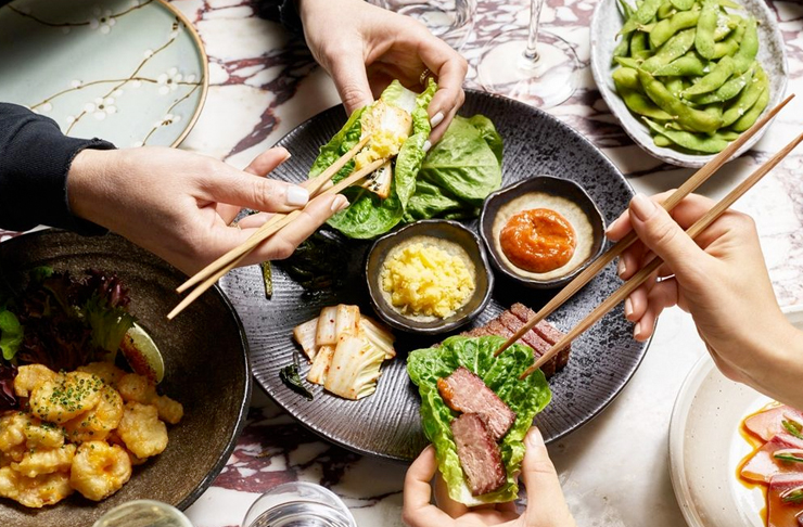 hands reaching over japanese feast with chopsticks