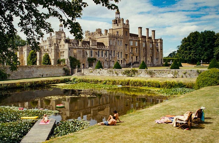 people relaxing near a pond on an estate with a castle