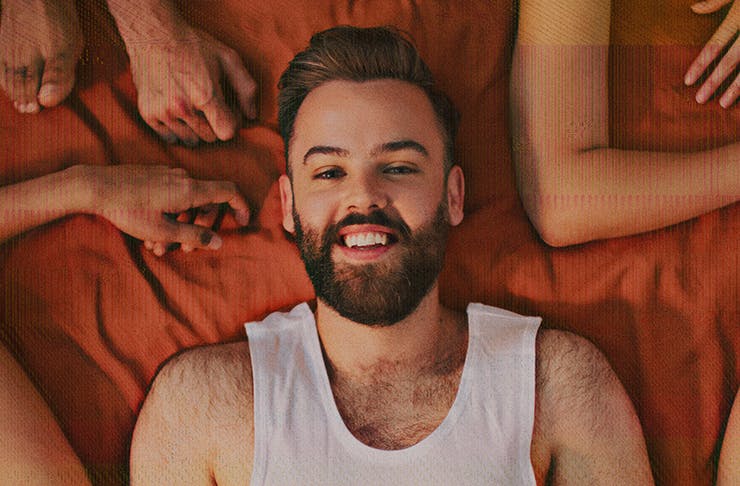 rowdie walden lying on bed sheet with arms framing him — host and creater of sex podcast search engine sex