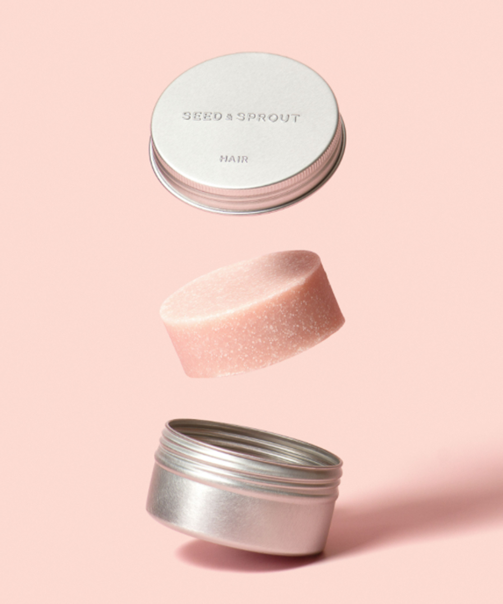 an open tin with a pale pink shampoo bar in between