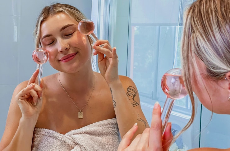woman using glass facial rollers on her face in the bathroom