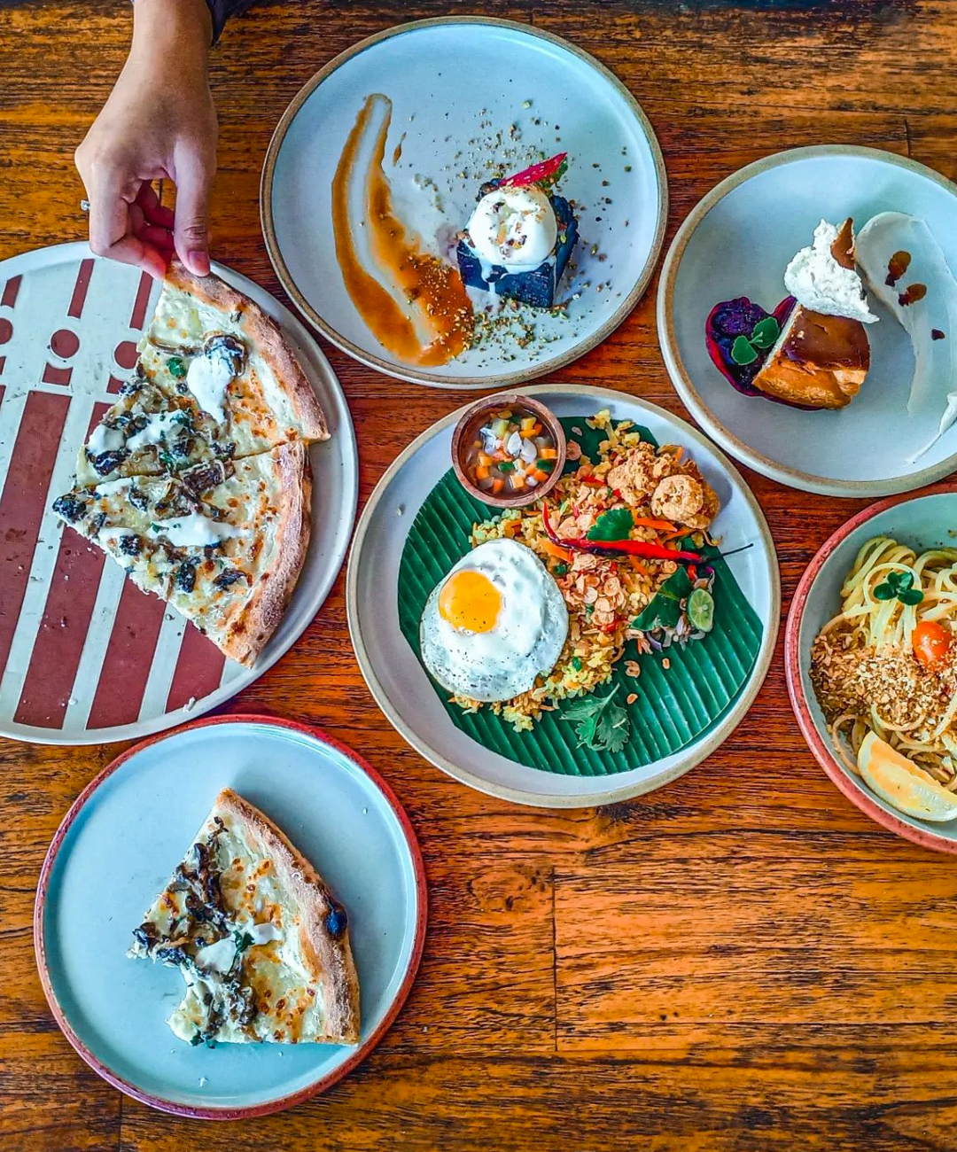 a spread of plates filled with food, a hand reaches over grabbing a slice of pizza