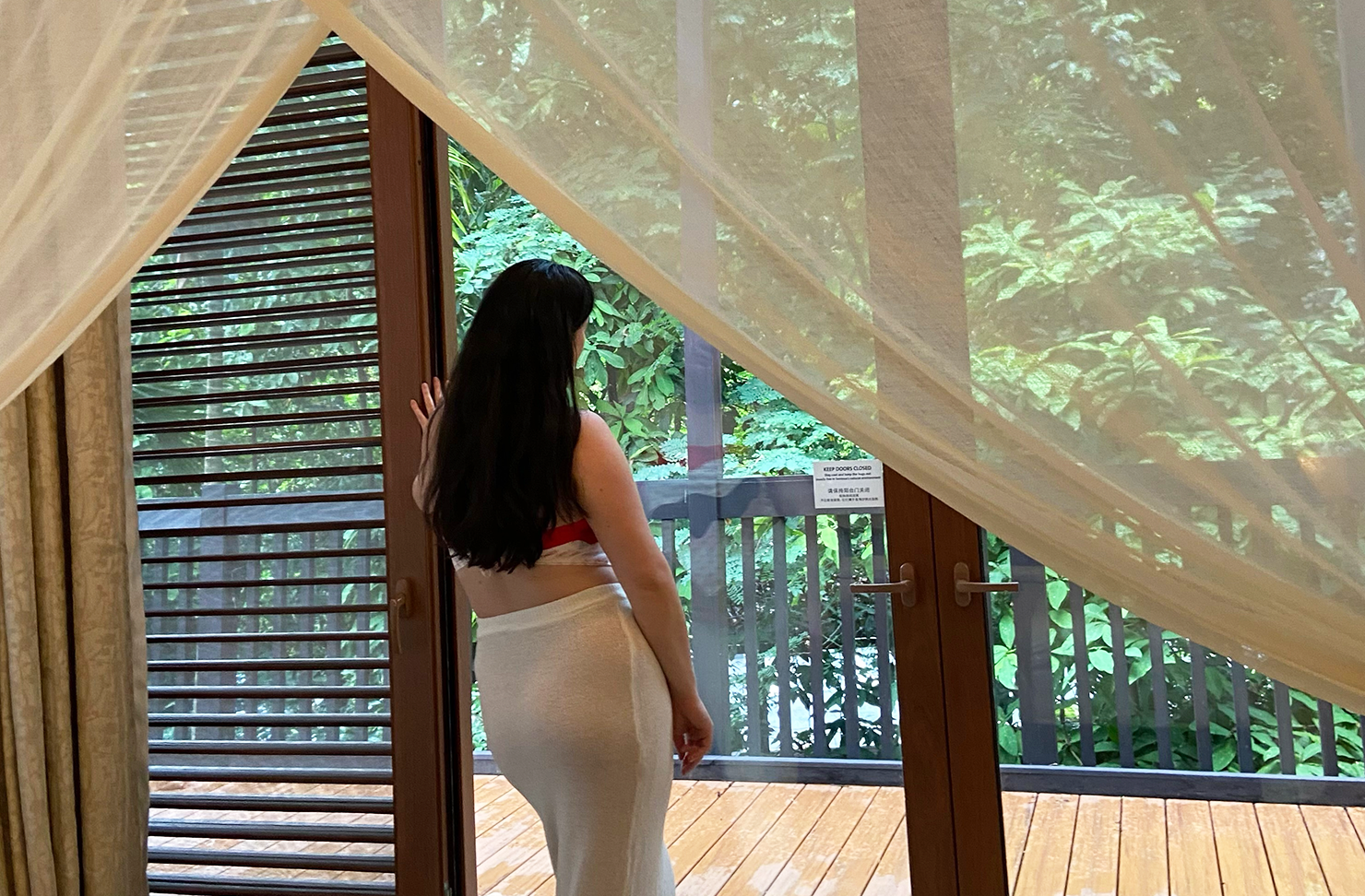 Woman in a hotel staring out the window to a garden. 