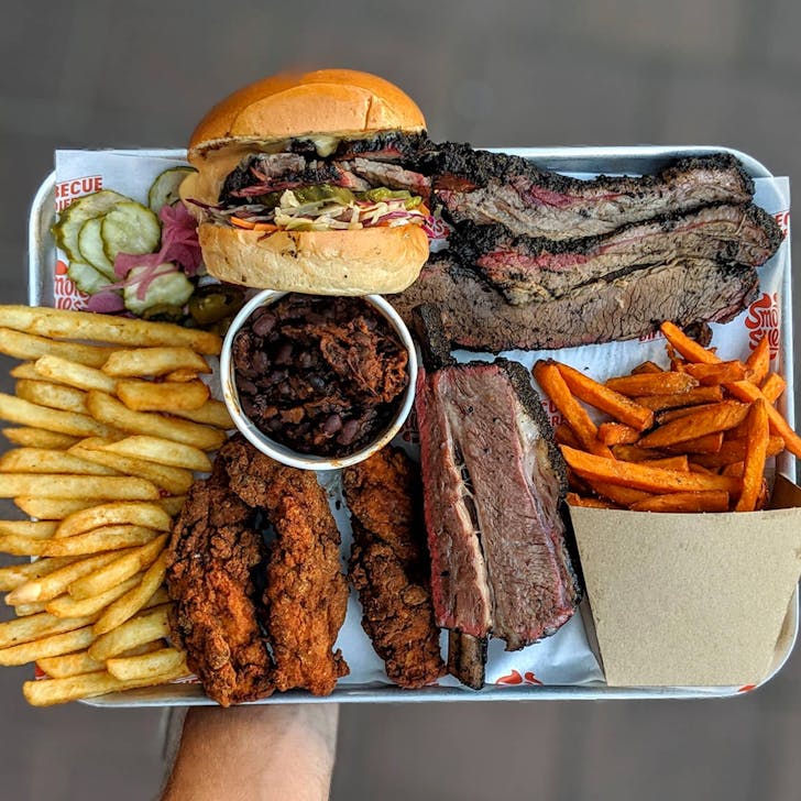 arm holding out big platter of smoked meats and hickory wings