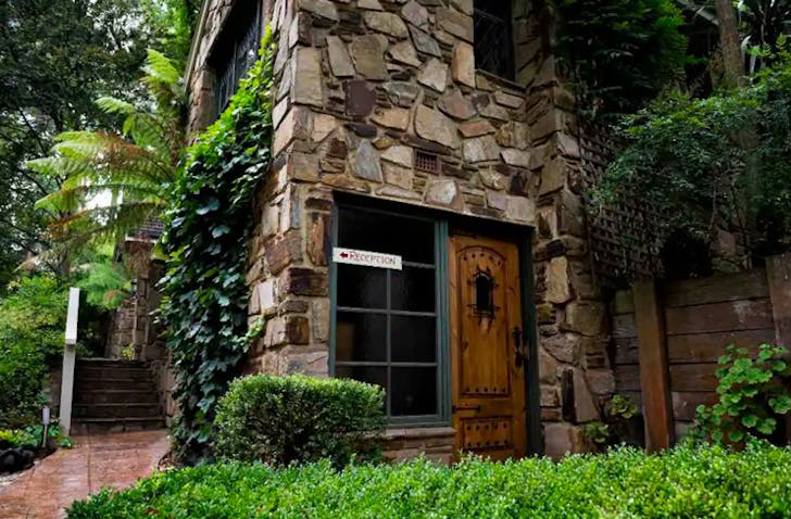 old chalet style building with vines and shrubs growing over it