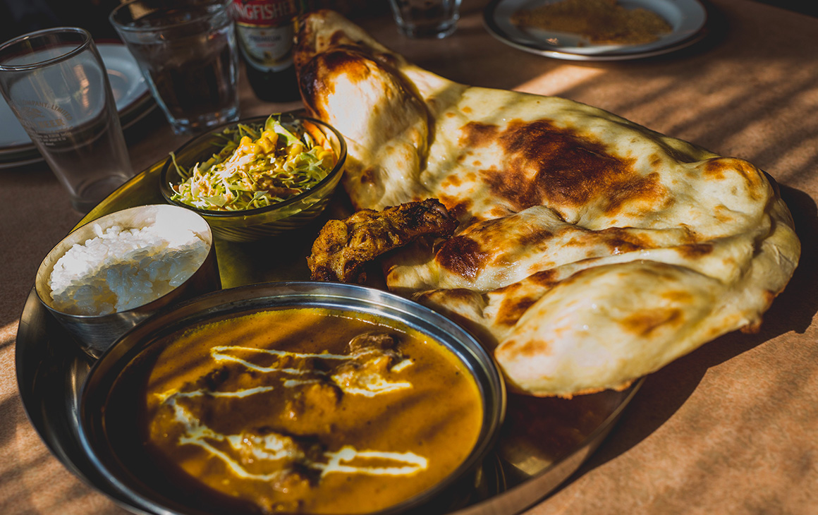 a curry, roti and drink sit on a tray in a cafe.