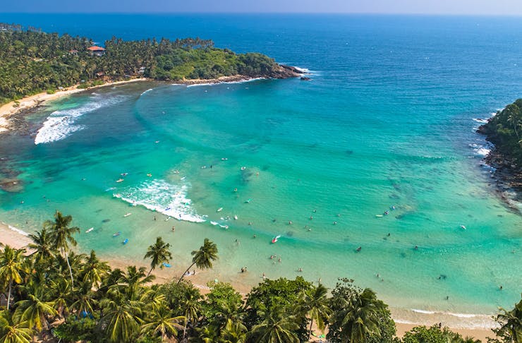 a stunning blue and green beach is fringed by palm trees.