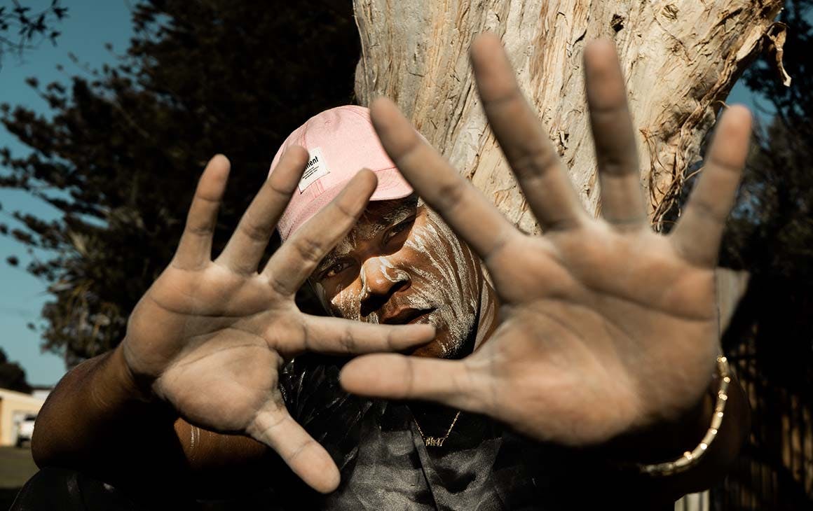 JK-47 wearing a pink hat, holds his hands up to the camera, blocking part of his face.