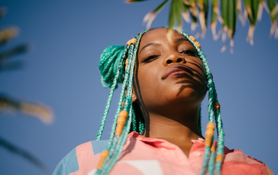 a woman with bright blue braids, looks up at the sky.
