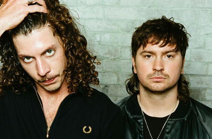 two men posing against a white brick wall