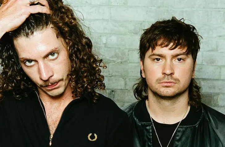 two men posing against a white brick wall