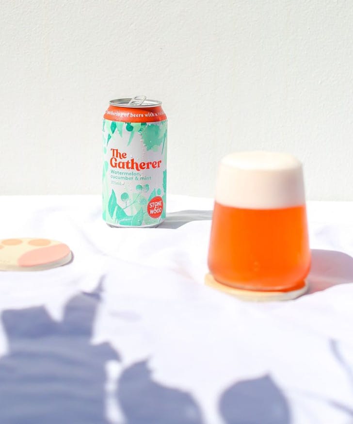 a glass of pink liquid sits next to a can of beer.