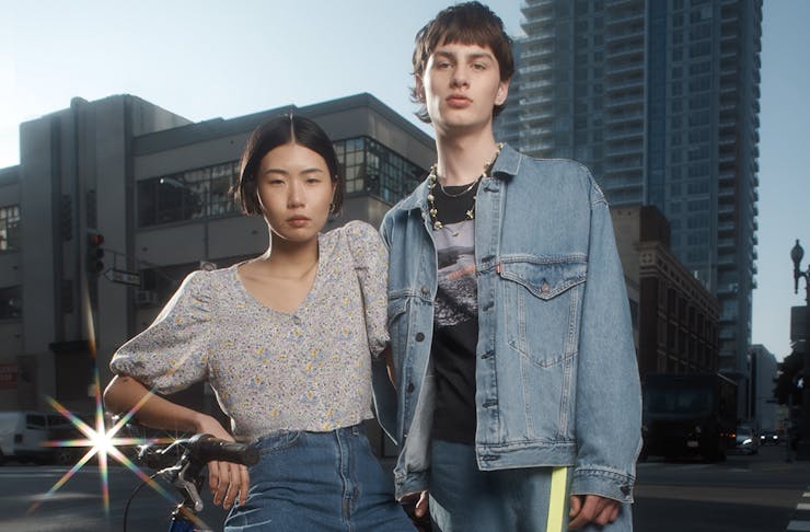 a young man and woman lean against a bike in a city.