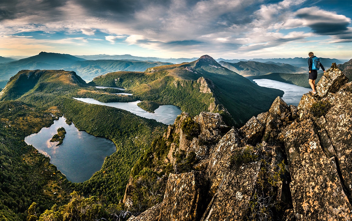 a heavy sky sits above rugged, rocky mountains. In the middle is still lake. 