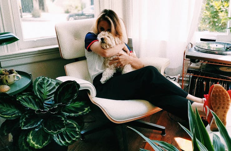 Woman sitting on a chair hugging a small dog with plants around her.