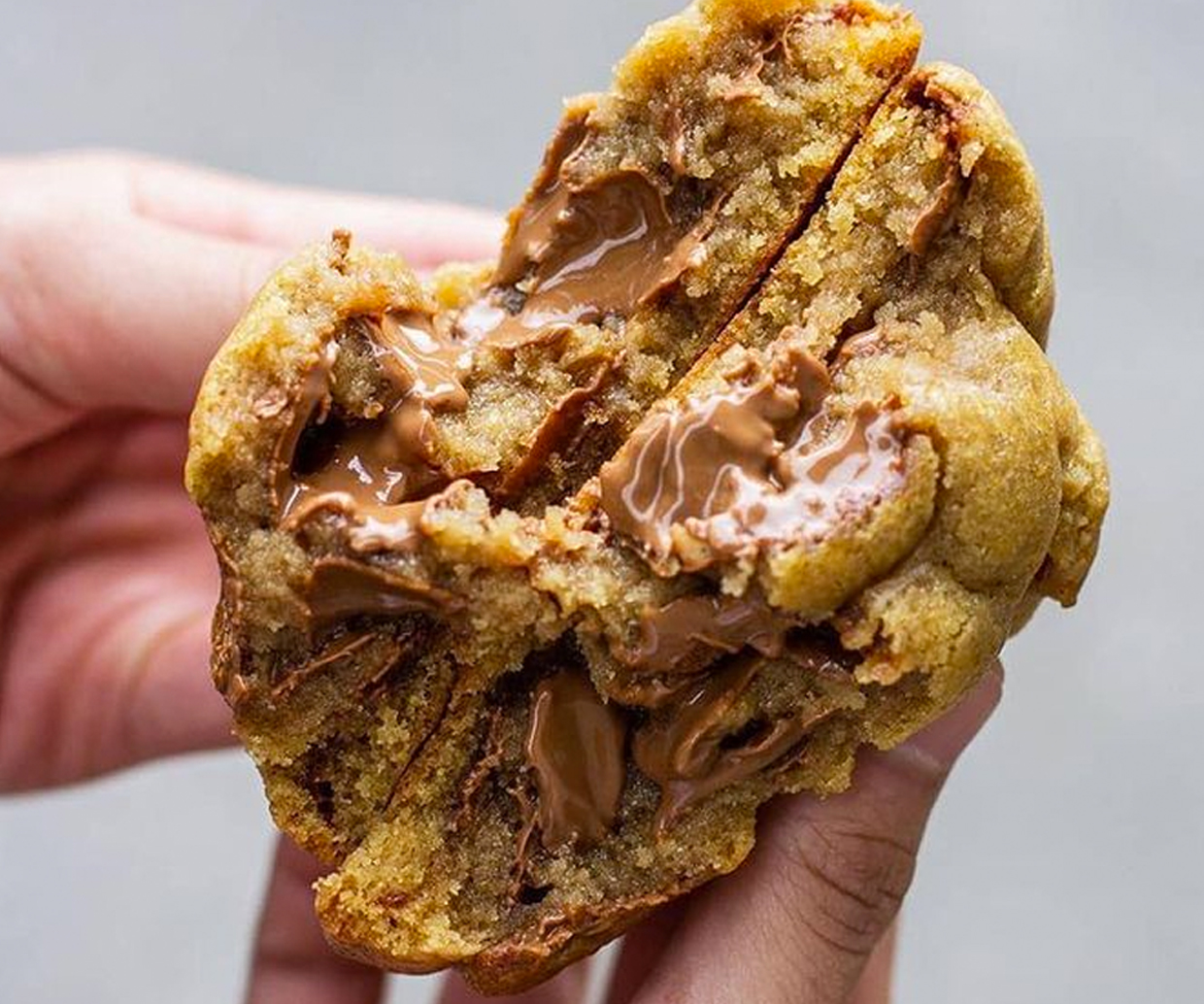 two hand holding halved of chunky cookie