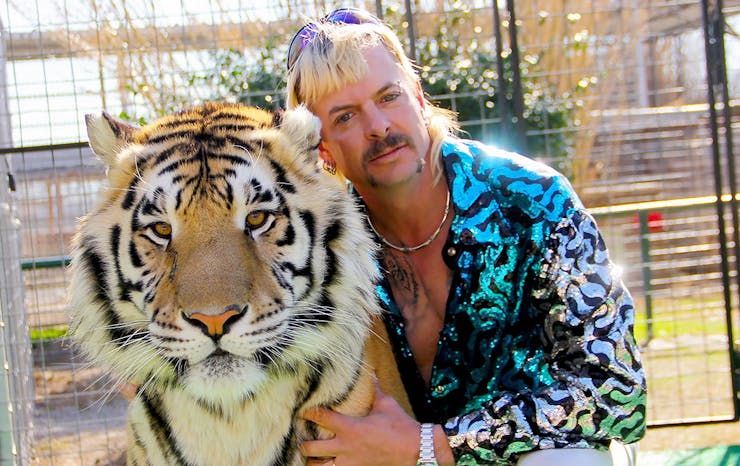 Tiger King, Joe Exotic, wears a blue shirt and cuddles up to a real tiger.