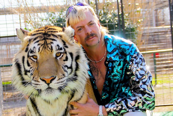 Tiger King, Joe Exotic, wears a blue shirt and cuddles up to a real tiger.