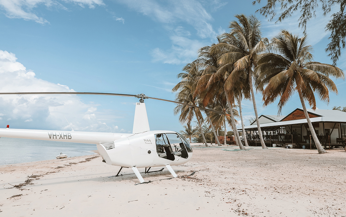 a white helicopter sits on a sandy beach outside the Tiwi Islands Retreat