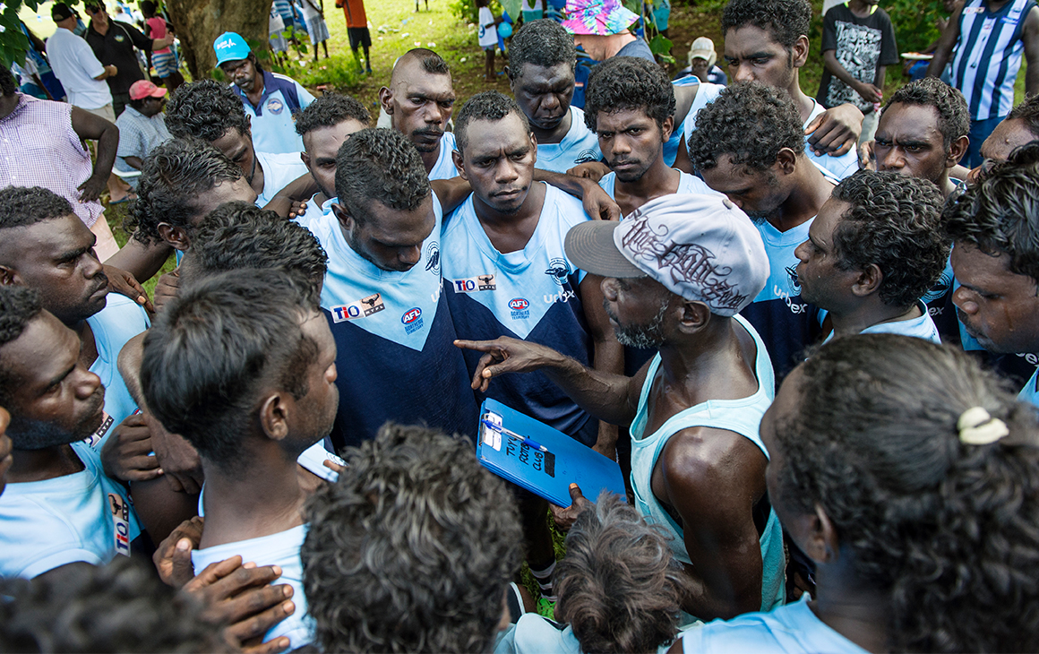 a cluster of AFL players huddle together ahead of the Tiwi Islands final