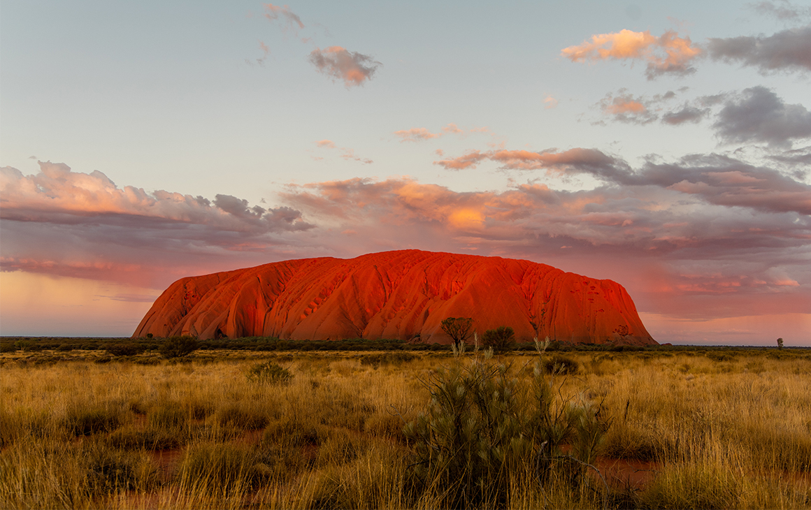 Uluru at sunset, a dusty pink and blue sky behind it.