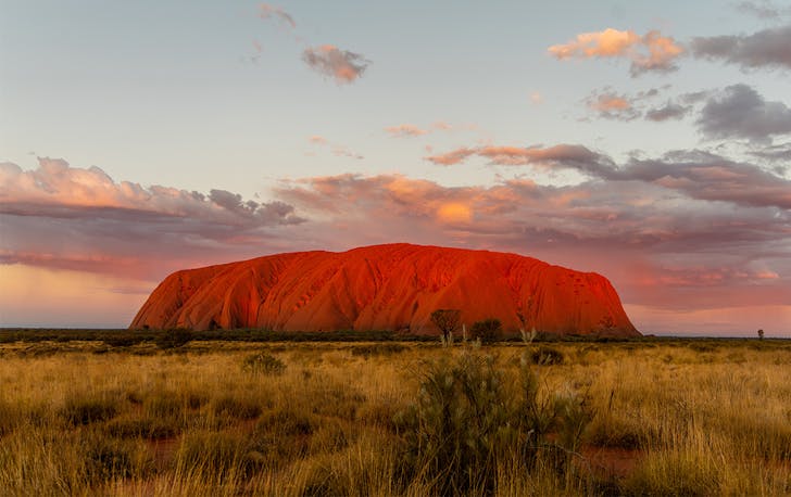 Uluru at sunset, a dusty pink and blue sky behind it.
