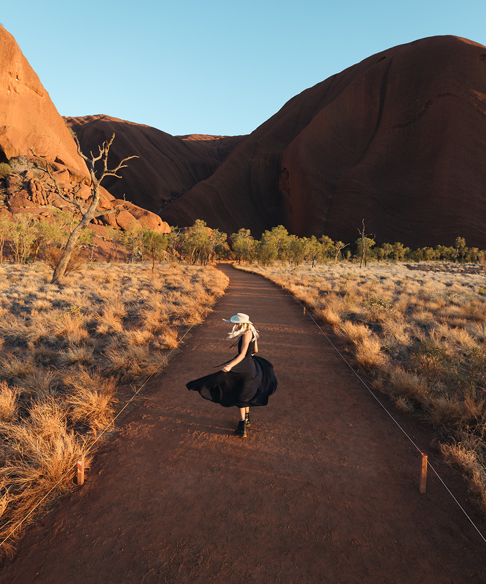 a woman in a black dress twirls in front of Uluru