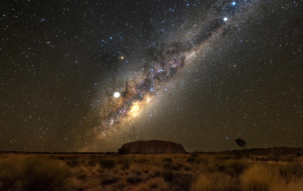 the night sky shimmers with stars over uluru at night.