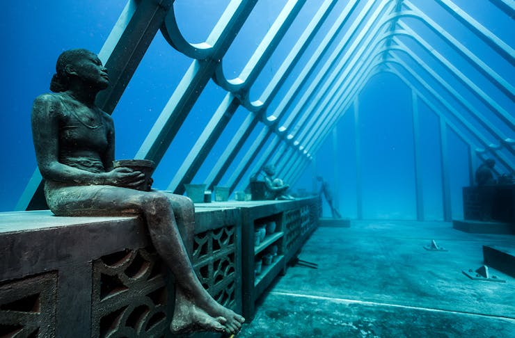 a stunning underwater sculpture featuring a woman sitting on a bench.