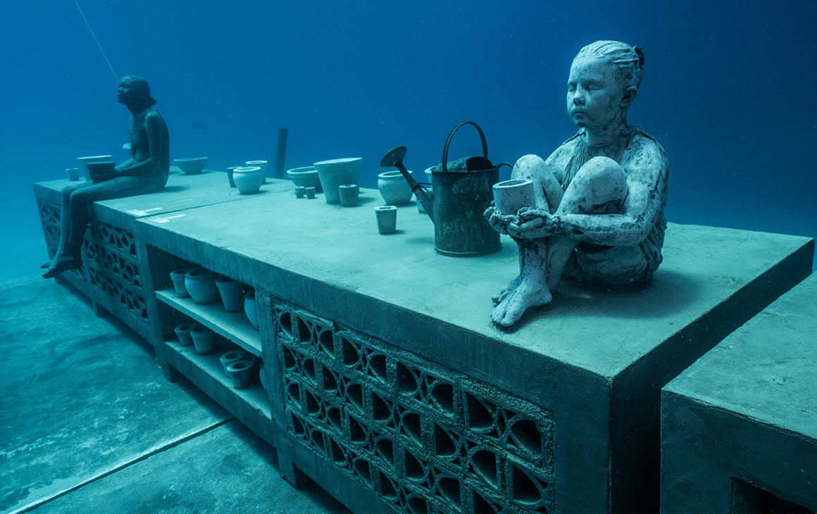 an underwater sculpture featuring a small child sitting on a bench and a woman in the backgound.