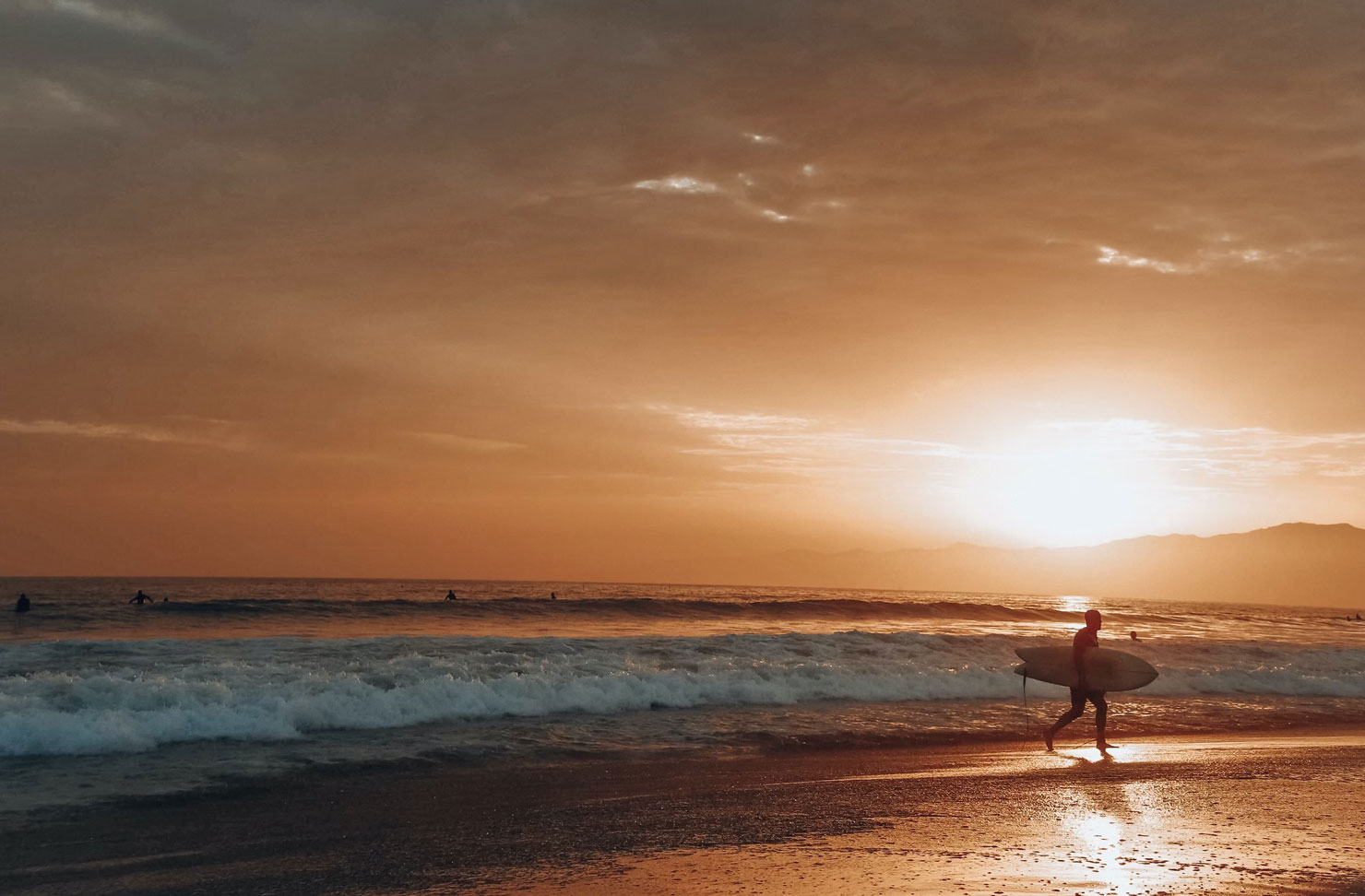 a person with a surfboard walking out of the ocean at sunset