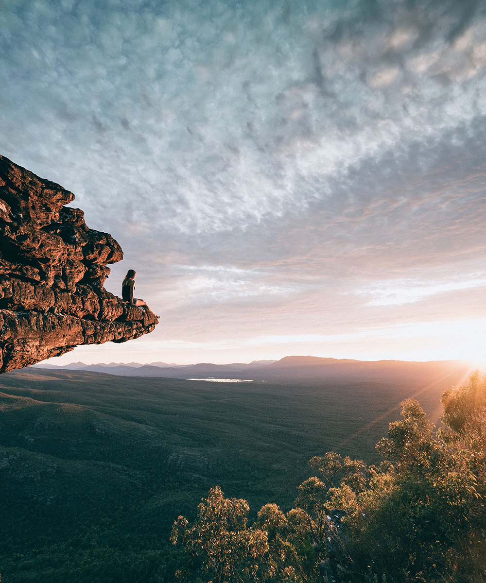 A woman sits on a rocky outcrop overlooking The Grampians